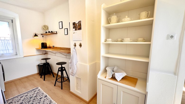 Helle Küche mit Regal, Barhockern und Kaffeemaschine.