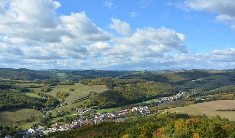 Landschaft mit Hügeln, Wäldern und einem Dorf im Herbst.