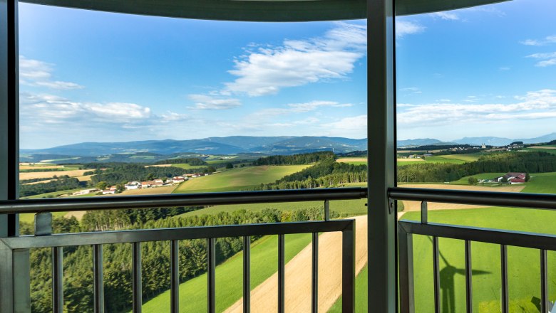 Aussicht von der Kanzel des Windrades aus auf eine grüne Landschaft mit Feldern und Hügeln unter blauem Himmel.