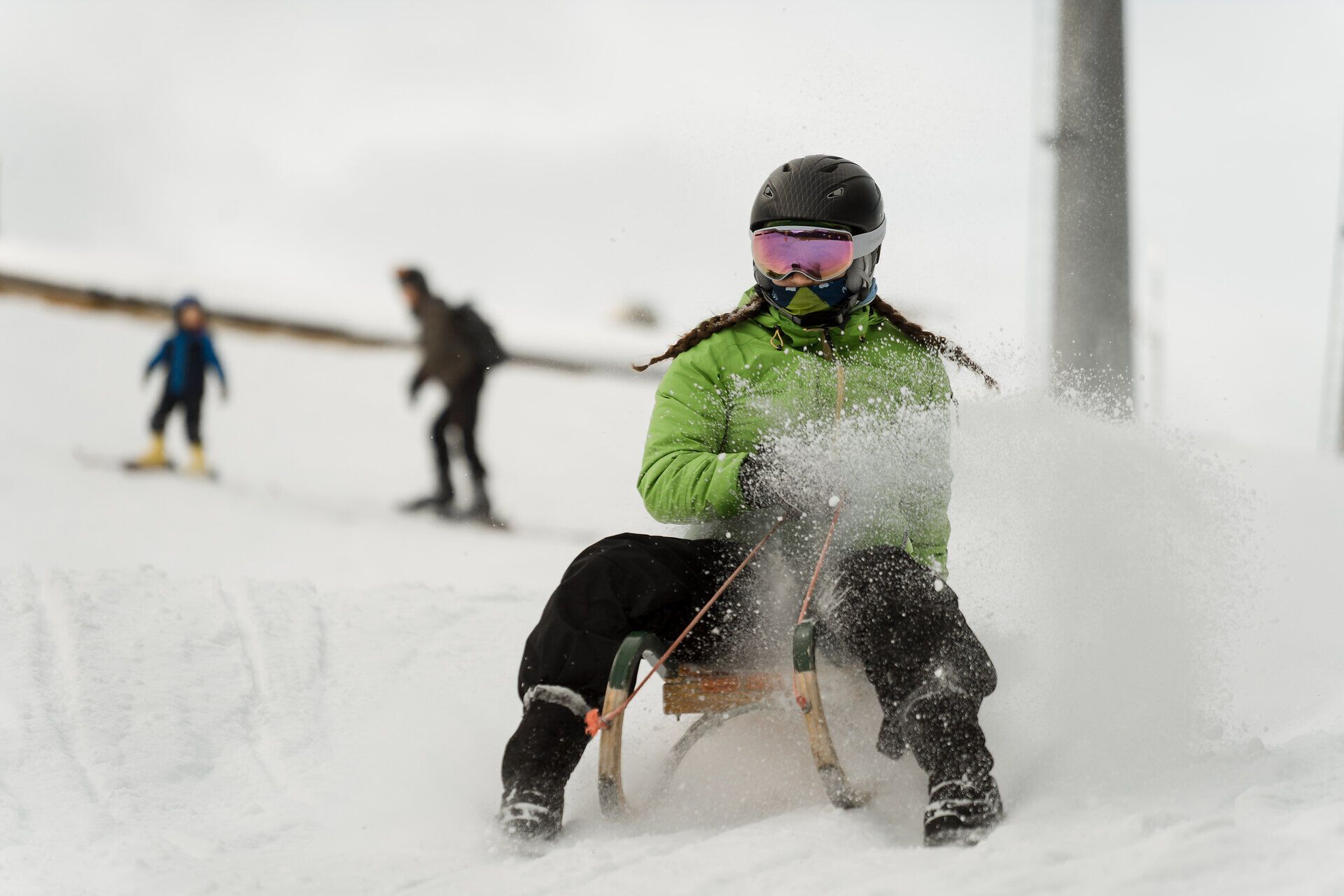 Eine Person in grüner Jacke rodelt durch den Schnee am Semmering Hirschenkogel.
