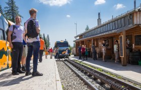 People at a station with a train and a wooden building.