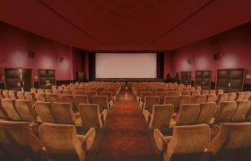 Leerer Kinosaal mit roten Wänden und beigen Sitzen und Leinwand