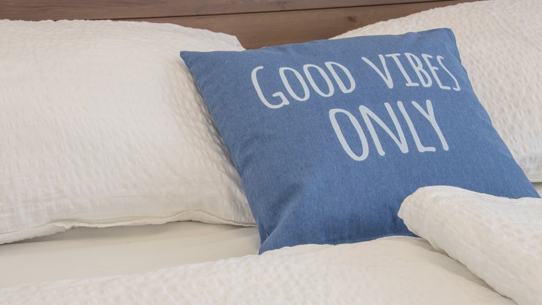 Bed with blue cushion, inscription 'Good Vibes Only'.
