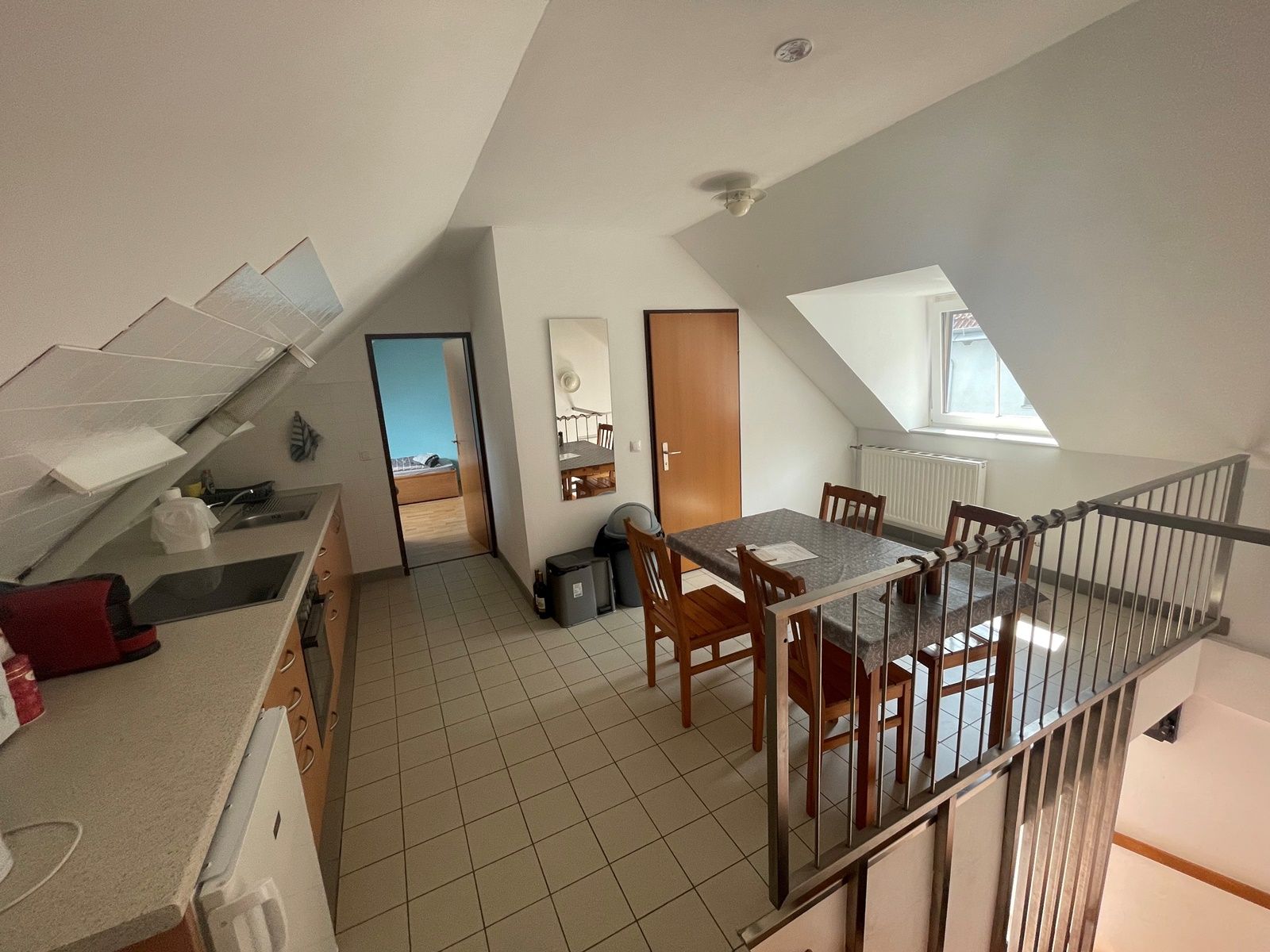 Wohnküche mit Esstisch, Stühlen, Küchenzeile und Dachschräge.