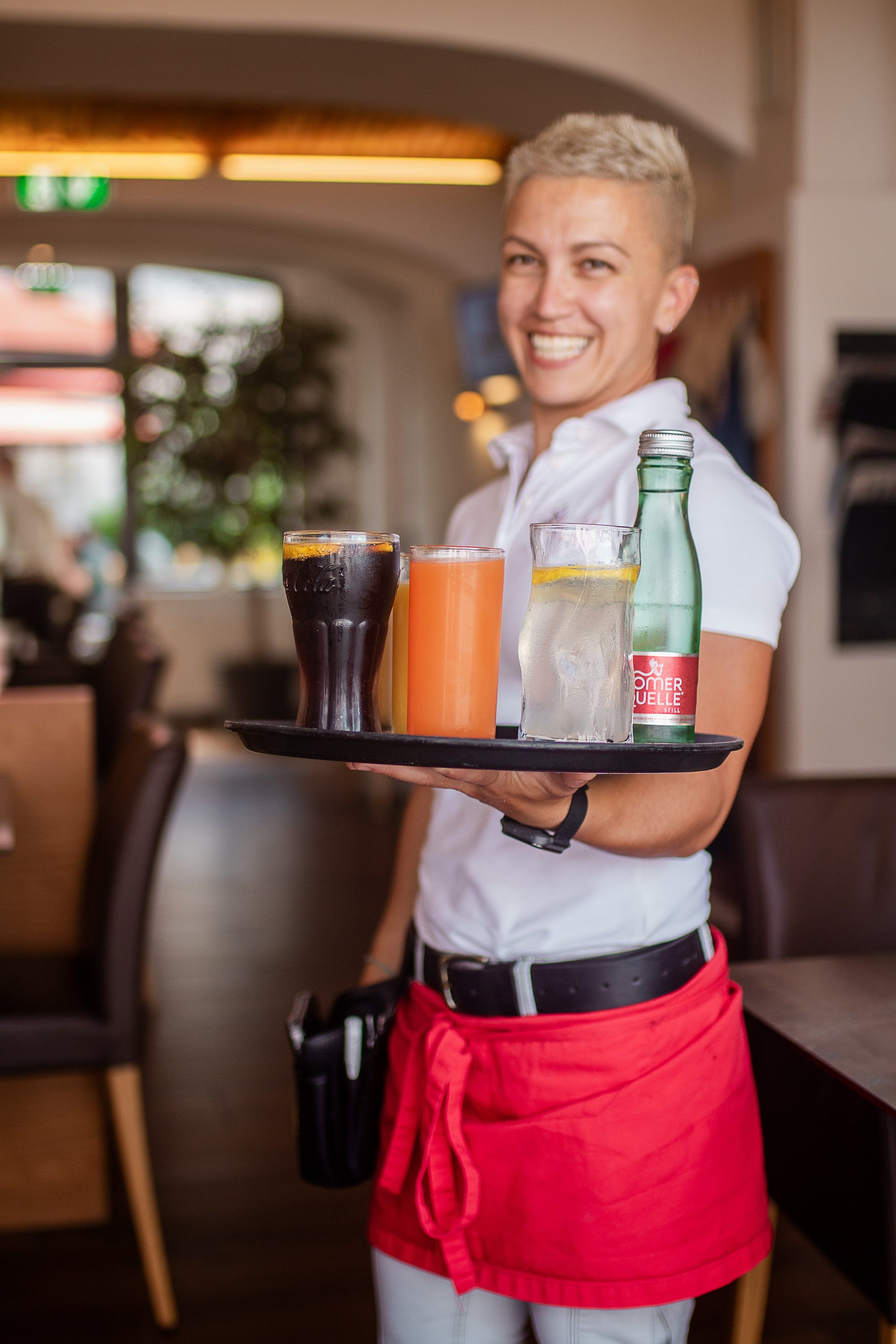 Eine lächelnde Kellnerin serviert Getränke auf einem Tablett in einem gemütlichen Restaurant.