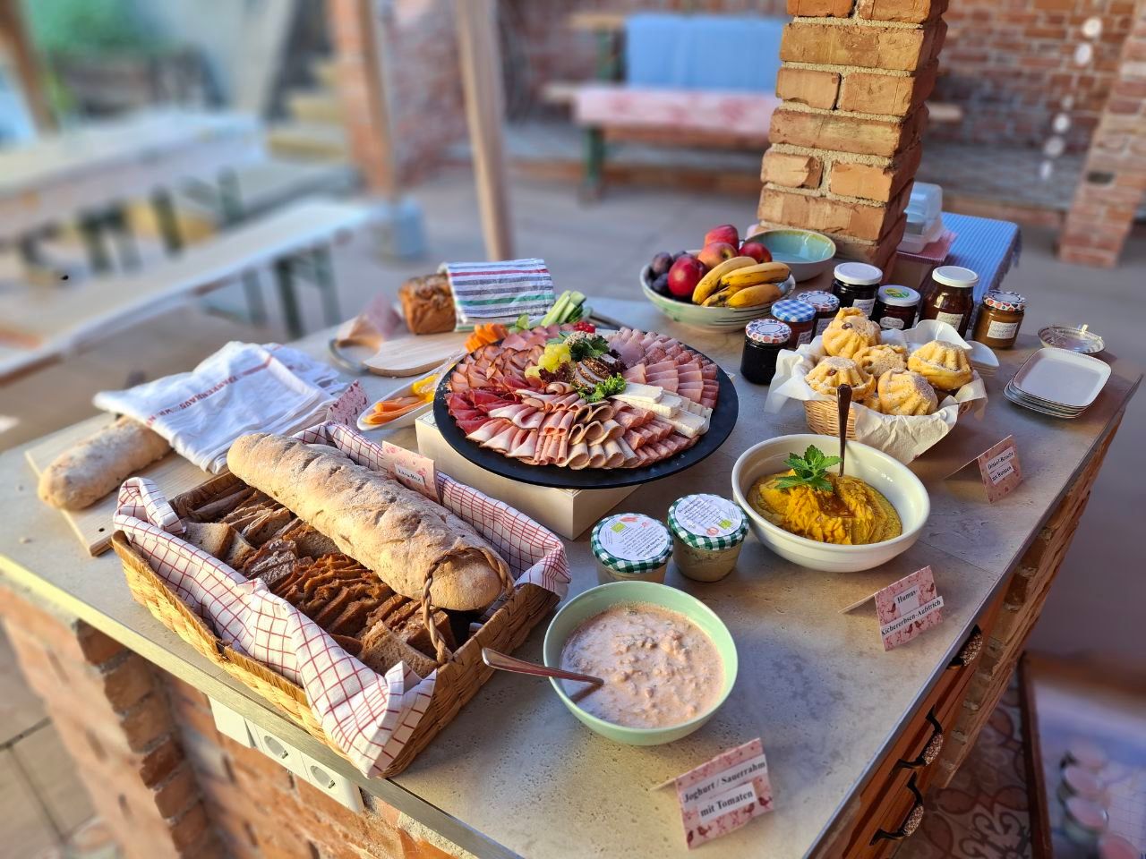 Ein Buffet mit Brot, Aufschnitt, Obst, Marmeladen und Dips auf einem Tisch.