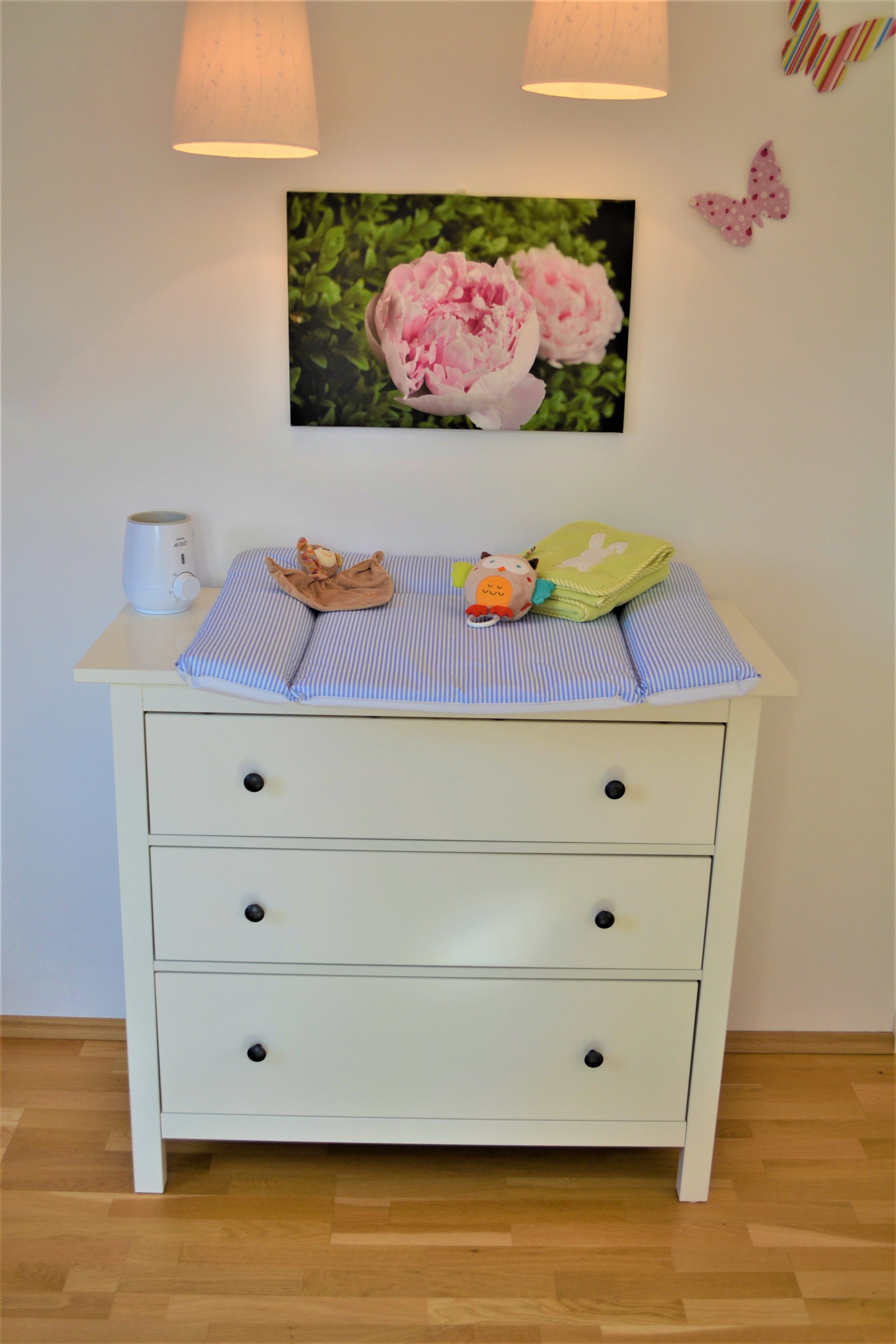 Wickeltisch mit blauer Auflage, Spielzeug und Dekorationen an der Wand.