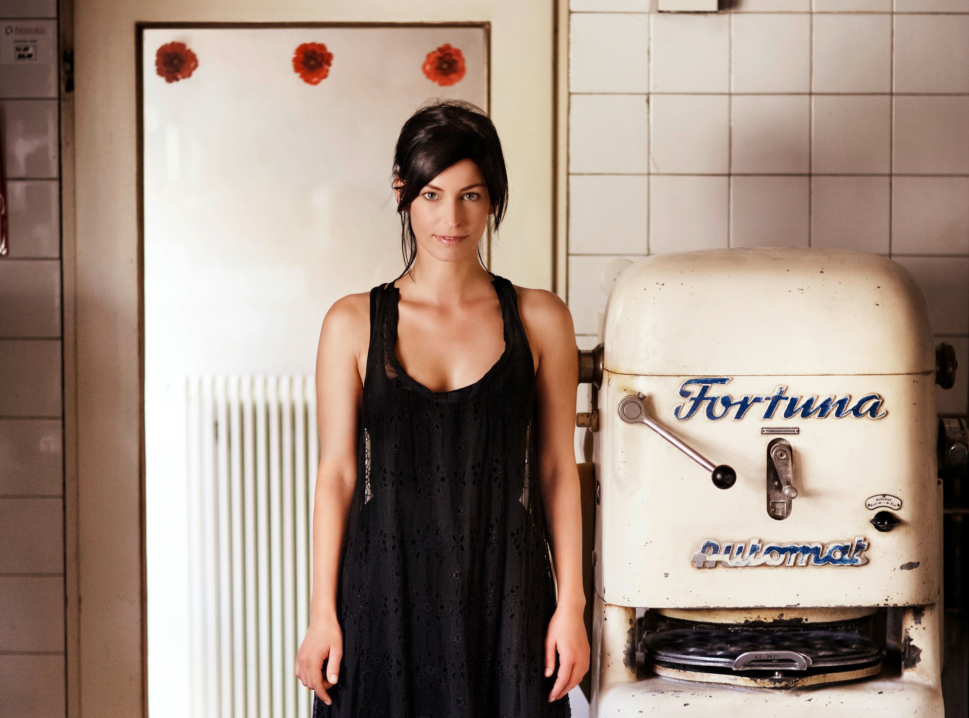 Eine Frau in einem schwarzen Kleid steht neben einer alten Bäckereimaschine mit der Aufschrift 'Fortuna'.
