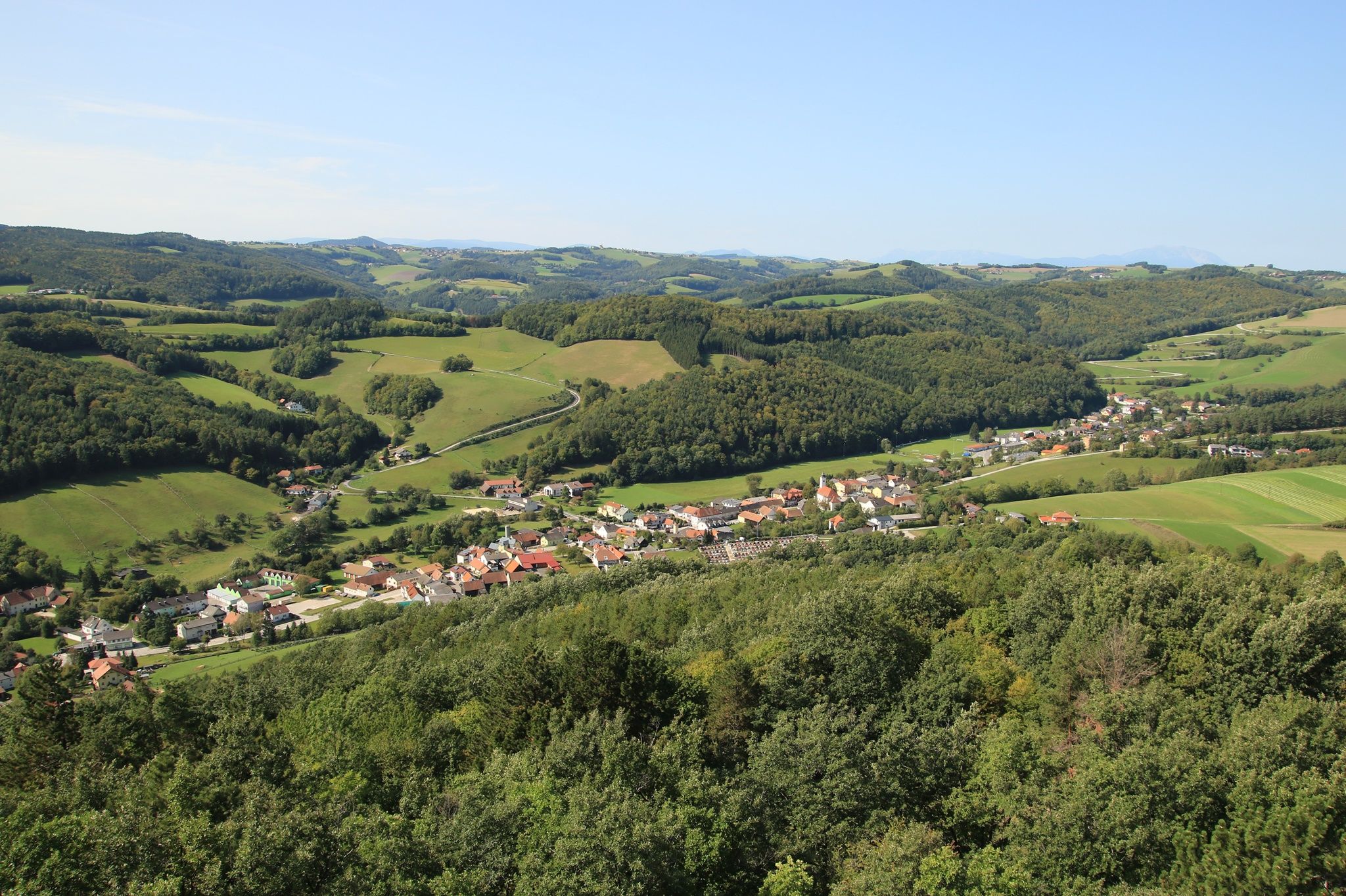 Panoramablick auf eine grüne Hügellandschaft mit einem Dorf im Vordergrund, aufgenommen vom Johann Giefing Aussichtsturm.