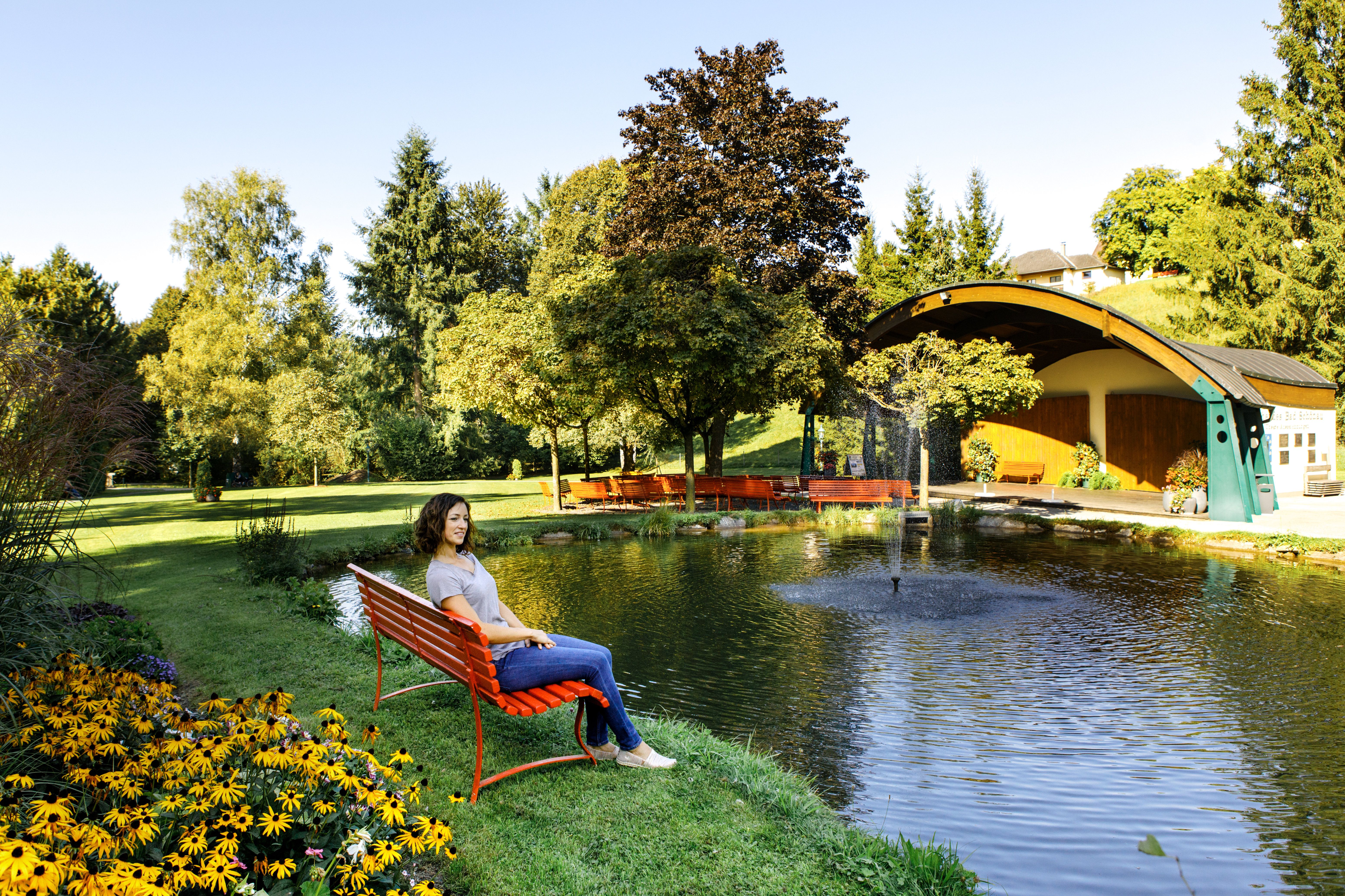 Frau sitzt auf einer roten Bank am Teich im Kurpark Bad Schönau.