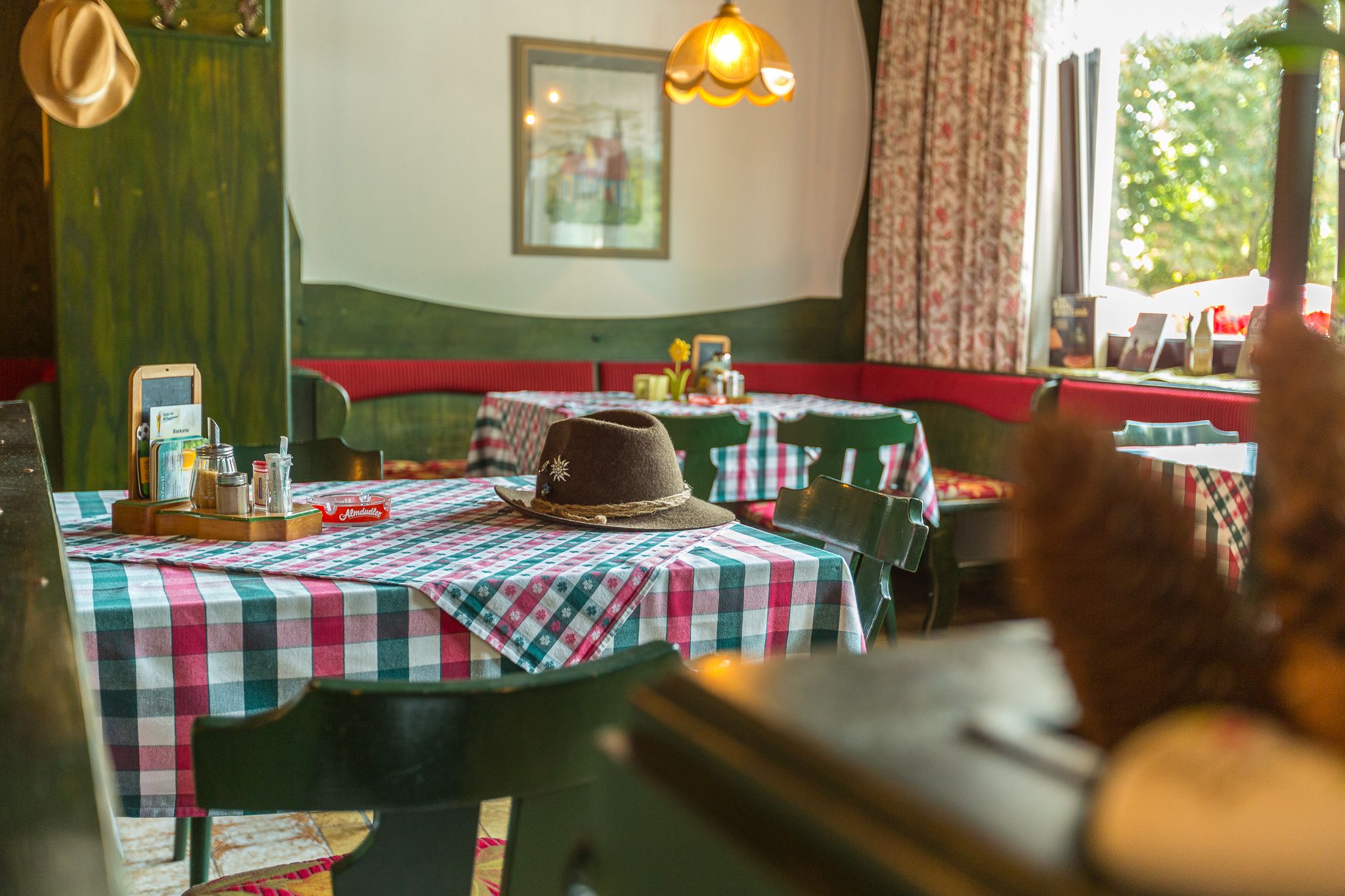 Gemütliche Gaststube mit karierten Tischdecken und einem Hut auf dem Tisch.