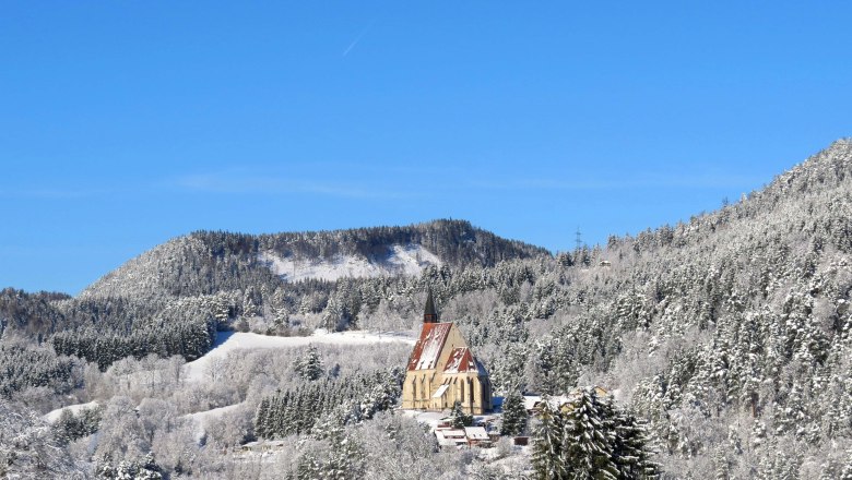 Winterlandschaft mit Kirche in verschneiten Bergen unter blauem Himmel.