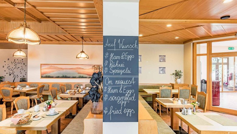 Frühstücksraum mit Holzmöbeln und einer Tafel mit Frühstücksoptionen.