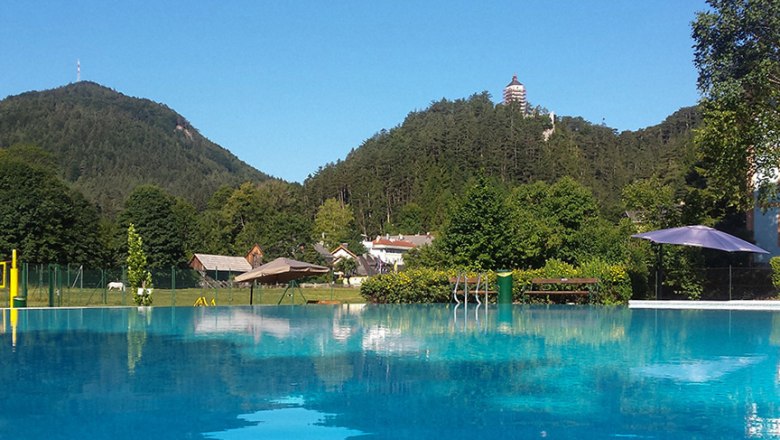 Freibad mit Blick auf bewaldete Hügel und einen Turm in der Ferne.