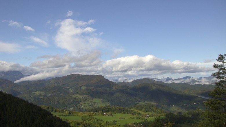 Panoramablick auf eine grüne Berglandschaft unter blauem Himmel mit Wolken.