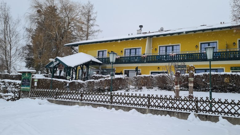 Yellow building in the snow with fence and trees.