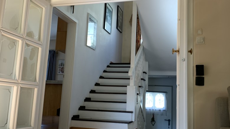 Interior view of a living room with wooden floor, stairs and open doors.