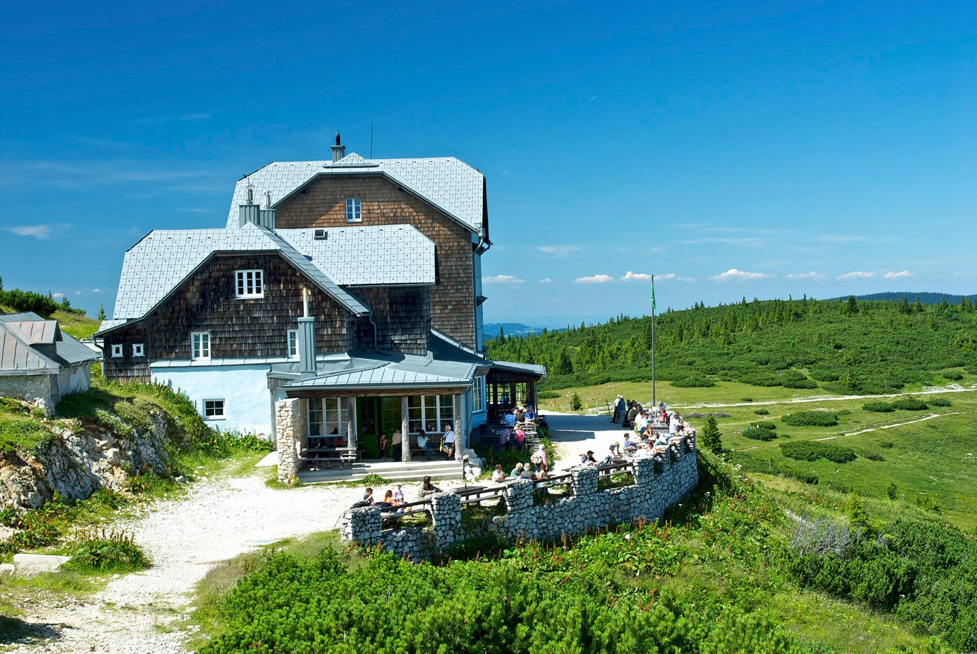 Das Ottohaus auf der Rax an einem sonnigen Tag mit blauen Himmel und grüner Landschaft.