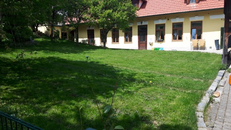 Grüner Garten vor einem gelben Gebäude mit roten Dachziegeln und mehreren Fenstern.