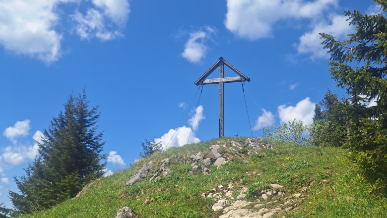 Gipfelkreuz auf einem Hügel mit blauem Himmel und Wolken.