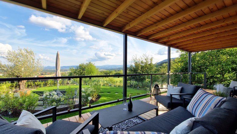 Covered terrace with modern furniture and views of the green landscape.