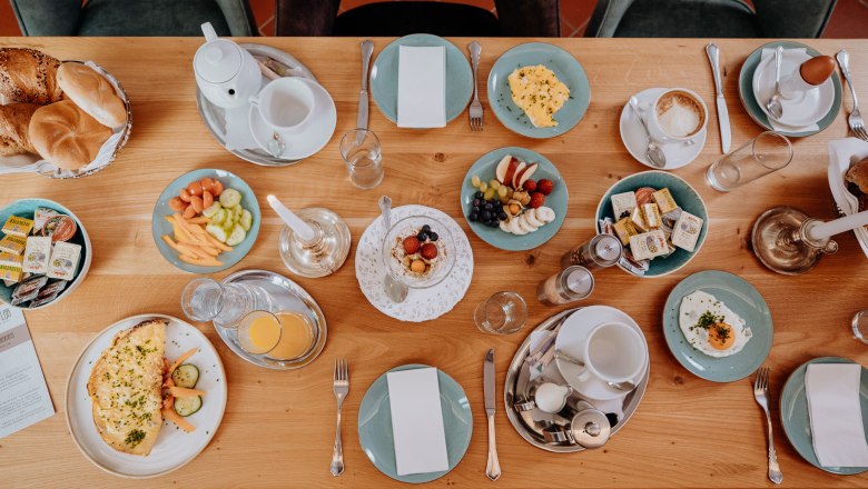 A laid breakfast table with bread rolls, eggs, fruit, omelette, juice and coffee.