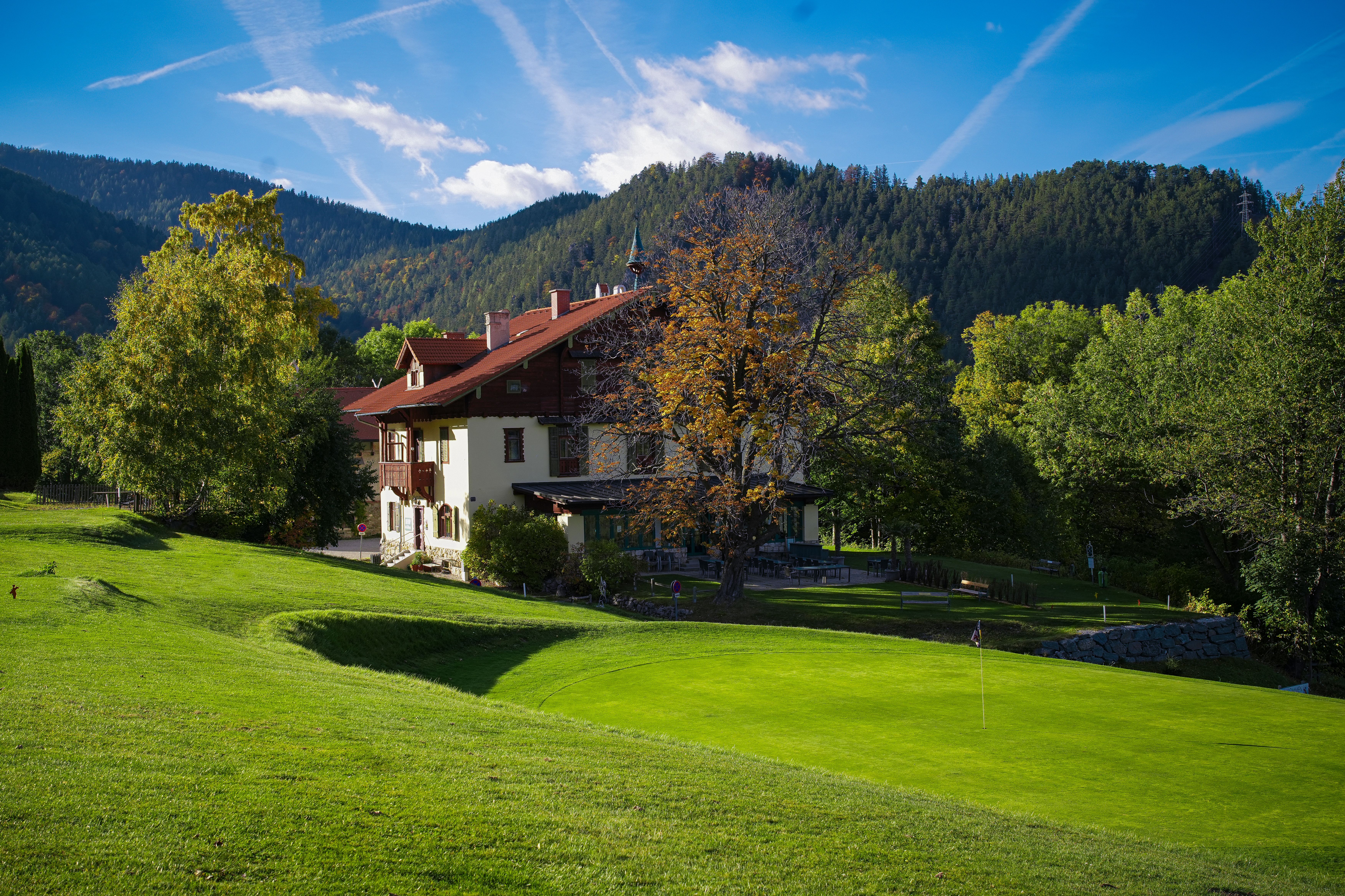 Clubhaus mit teilweise Holzverkleidung in mitten grüner Natur, umgeben von Bäumen und Hügeln im Hintergrund