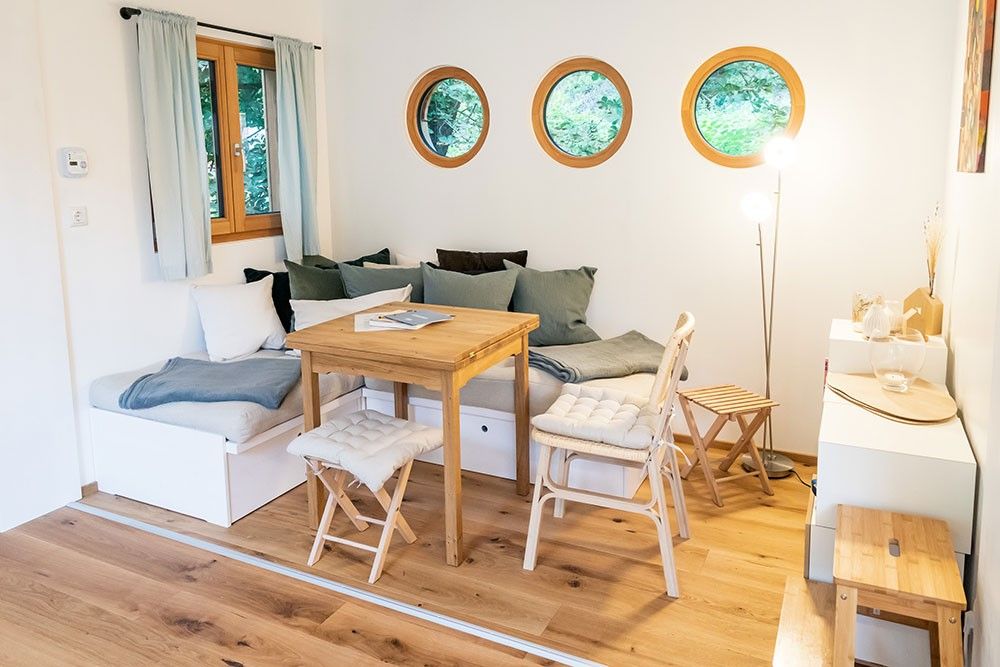 Gemütlicher Sitzbereich mit Holztisch, Stühlen und runden Fenstern.