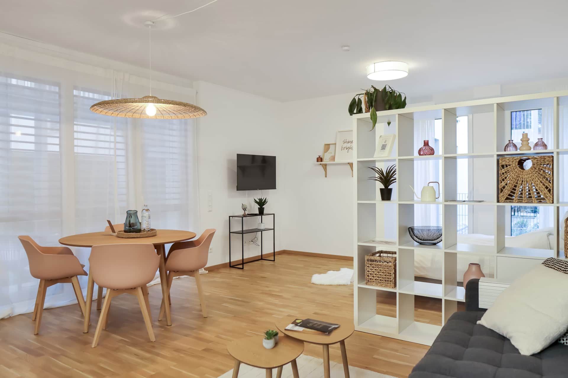Helles Wohnzimmer mit grauer Couch, Raumteiler, Esstisch und beigen Wänden