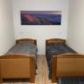 A simply furnished room with two single beds and a landscape painting on the wall.