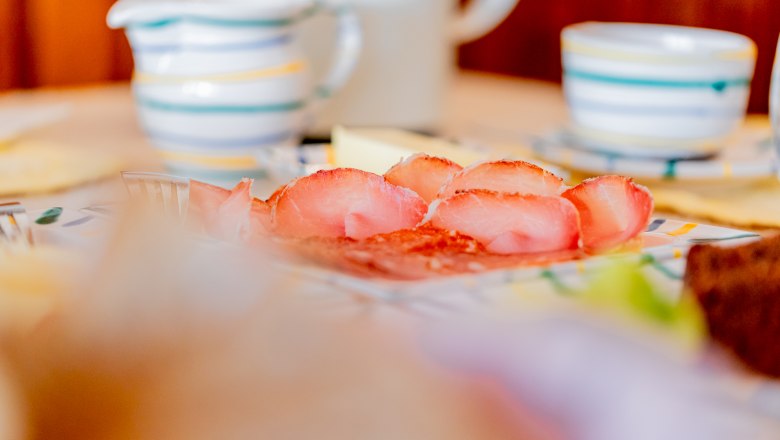 Close-up of a breakfast table with ham, crockery and cups.