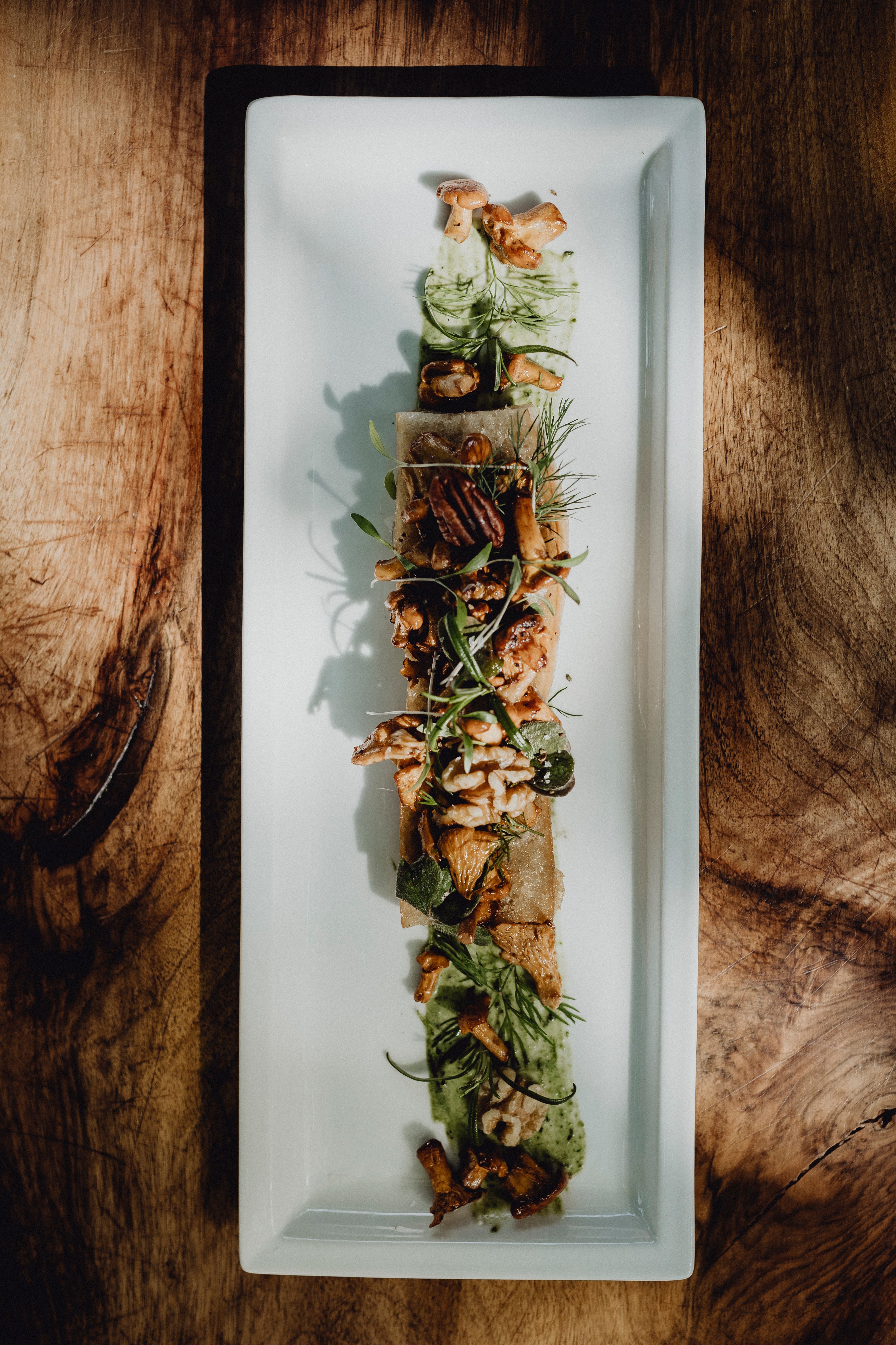 Ein Gourmetgericht auf einem rechteckigen Teller, garniert mit Nüssen und Kräutern.