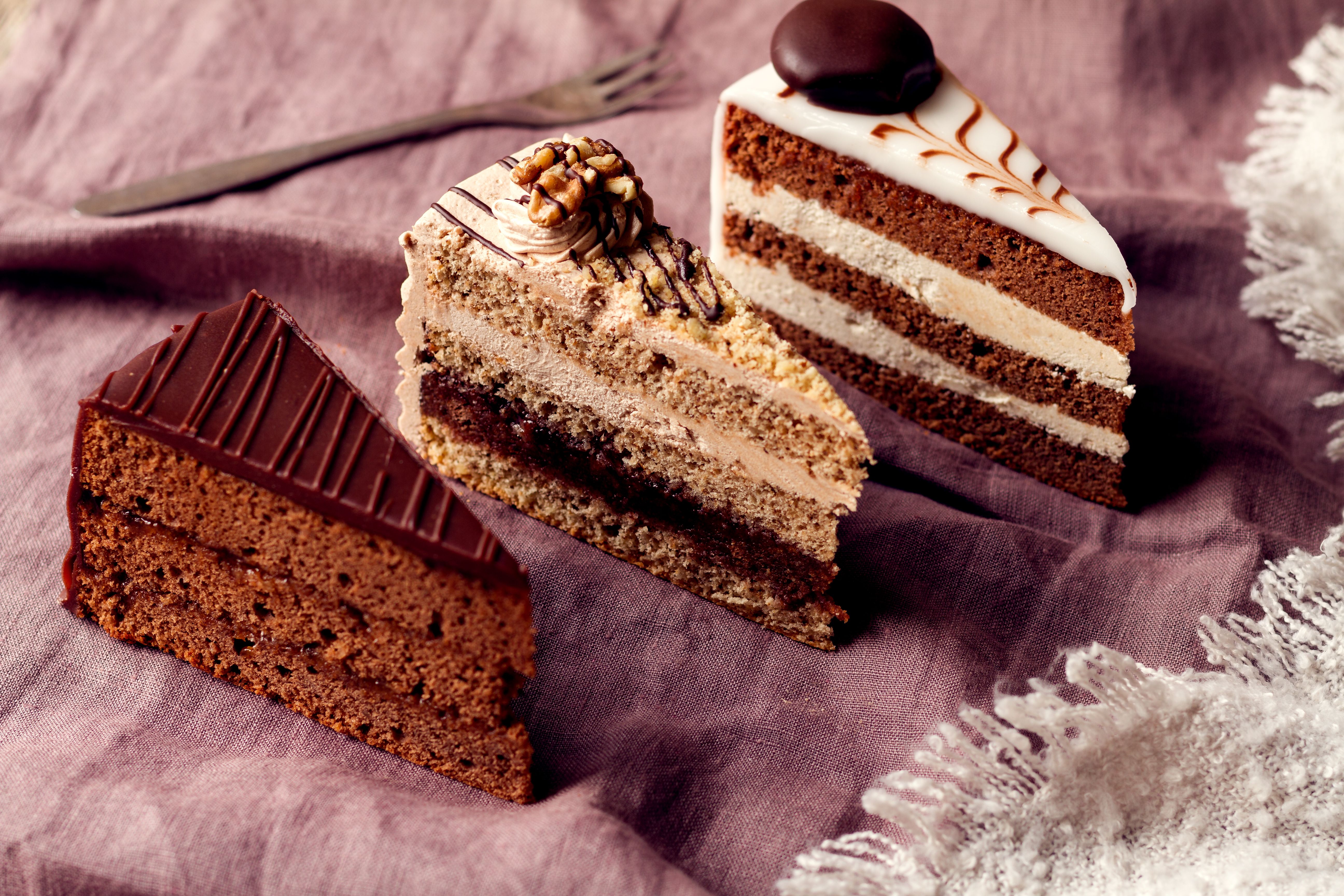 Drei verschiedene Tortenstücke auf einem lila Tuch.