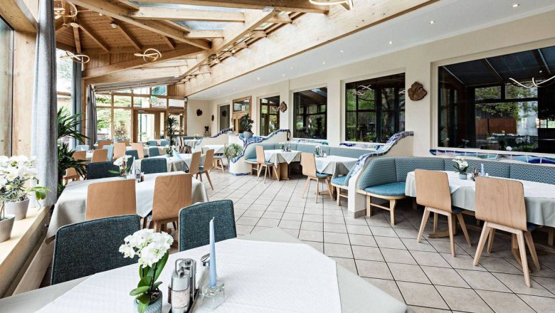 Ein heller Wintergarten mit gedeckten Tischen und Holzmöbeln.