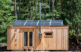 Kleines Holzhaus mit Solarpanelen auf dem Dach im Wald.