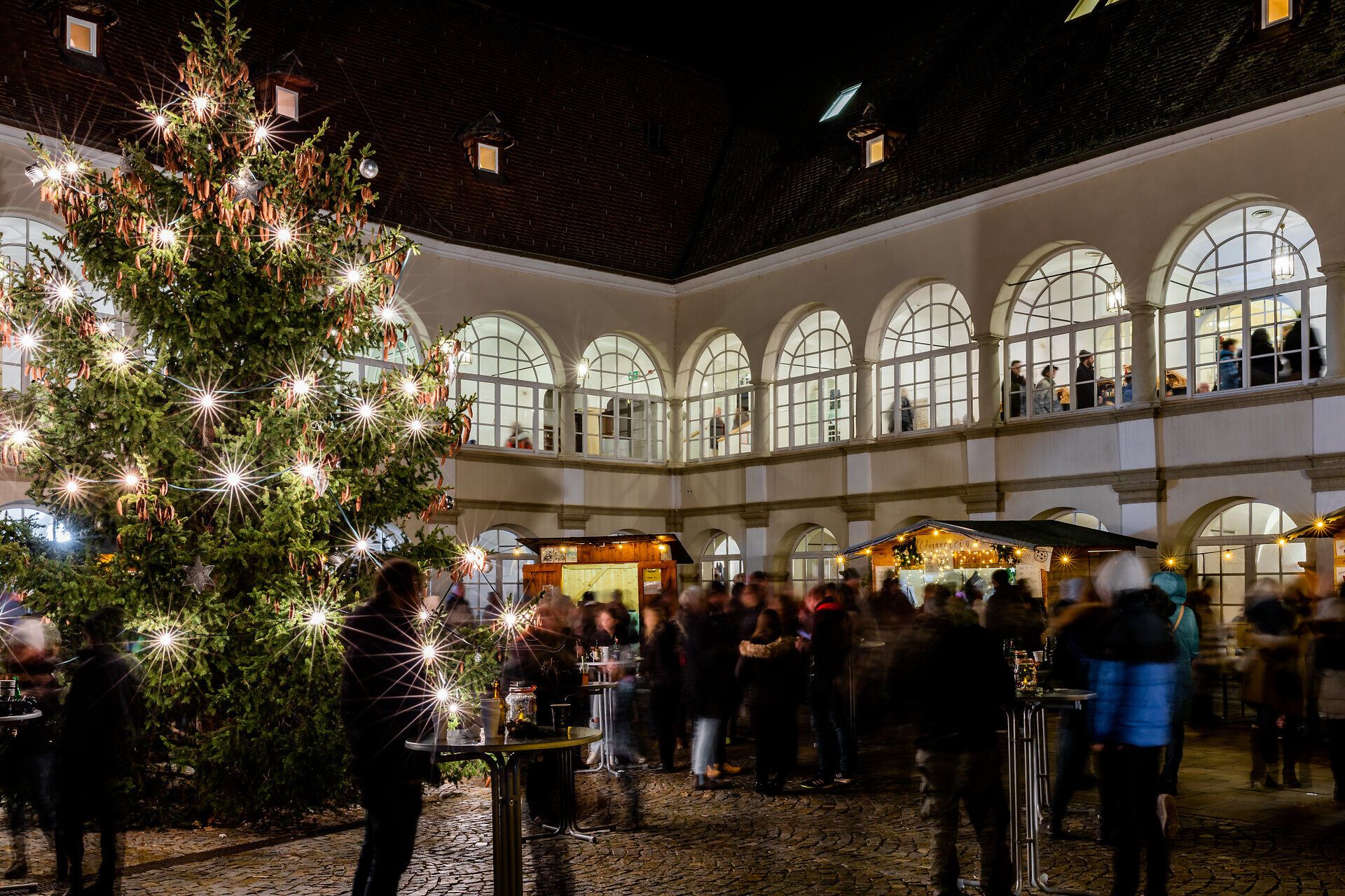 Großer Weihnachtsbaum in einem historischen Innenhof mit vielen Besuchern bei Nacht.