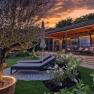 Ein modernes Chalet mit Terrasse und Liegest&uuml;hlen im Garten bei Sonnenuntergang.