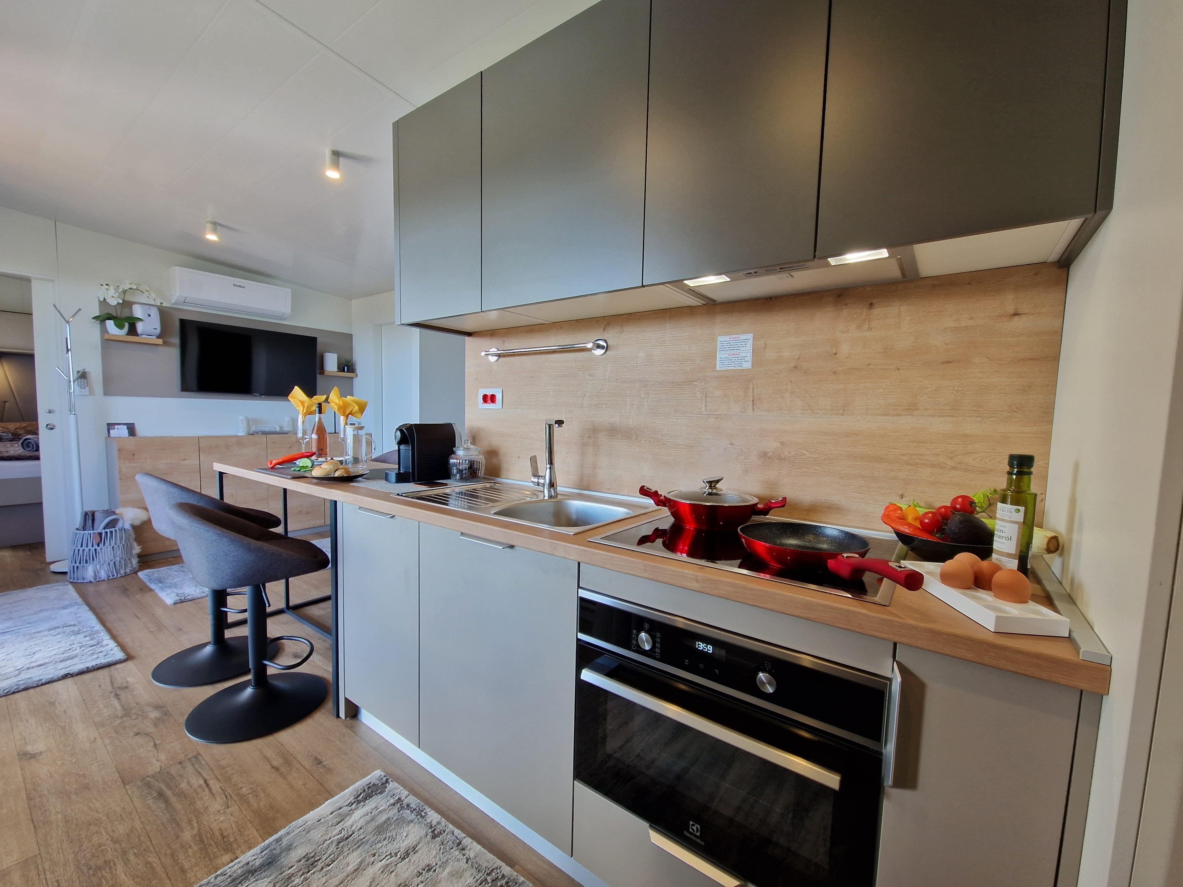 Moderne Küche mit grauen Schränken, Herd, Spüle und Barhockern.