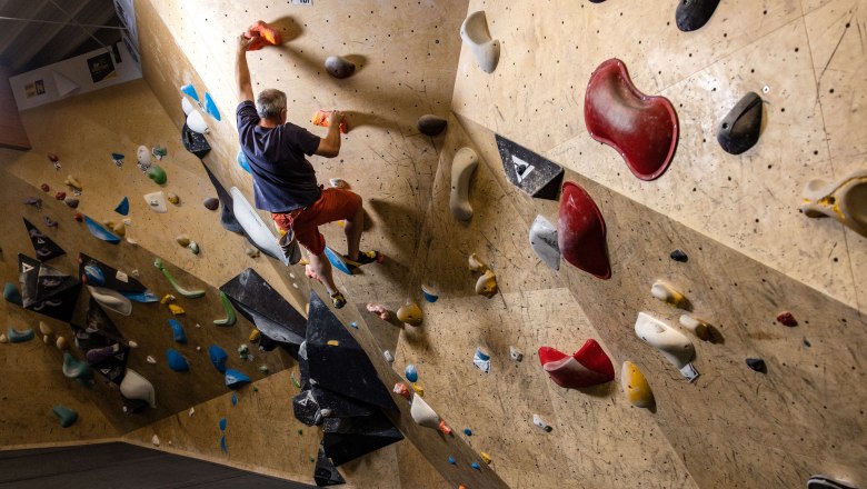 Person beim Bouldern an einer Kletterwand mit bunten Griffen.