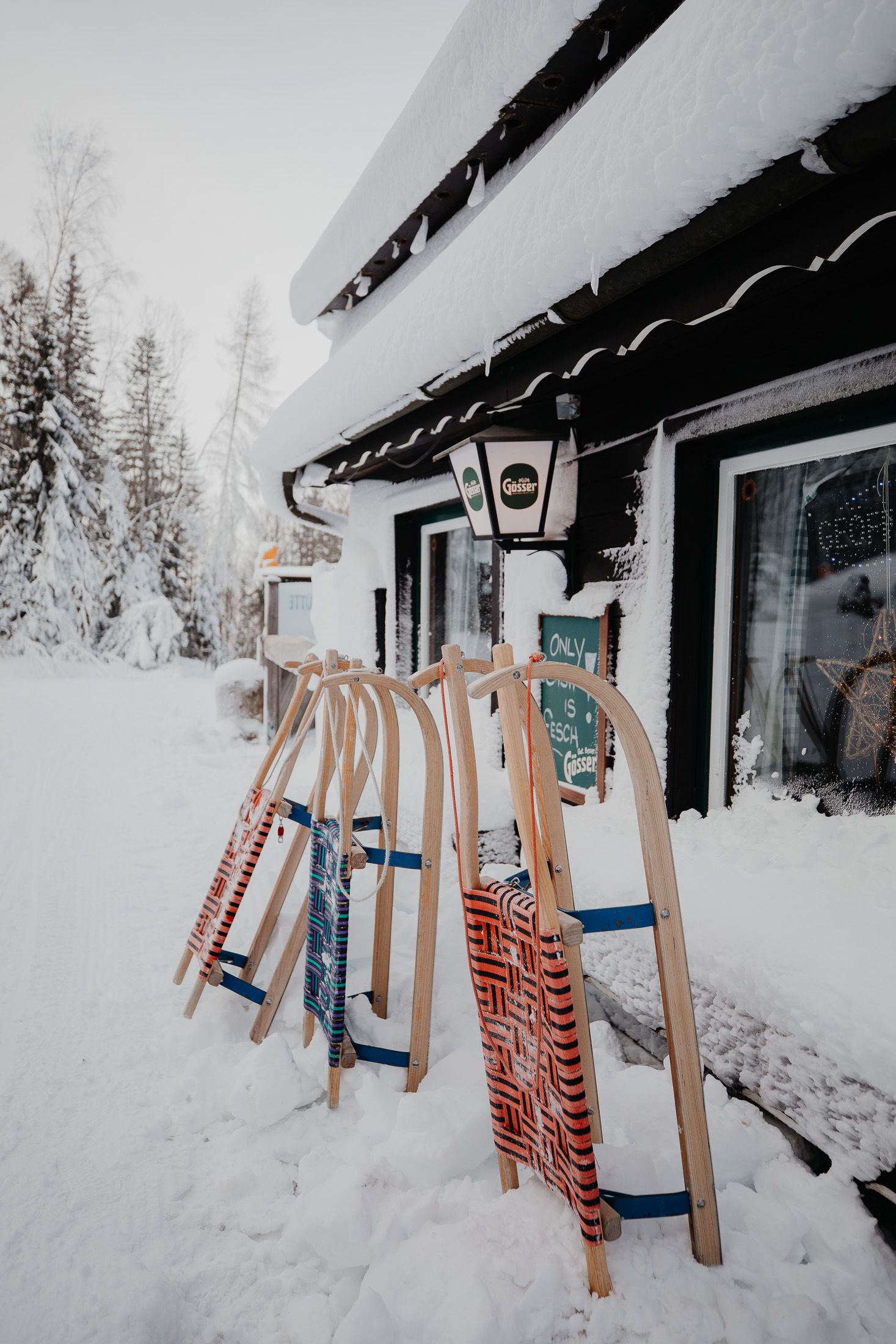 drei Rodeln stehen vor der verschneiten Holzhütte