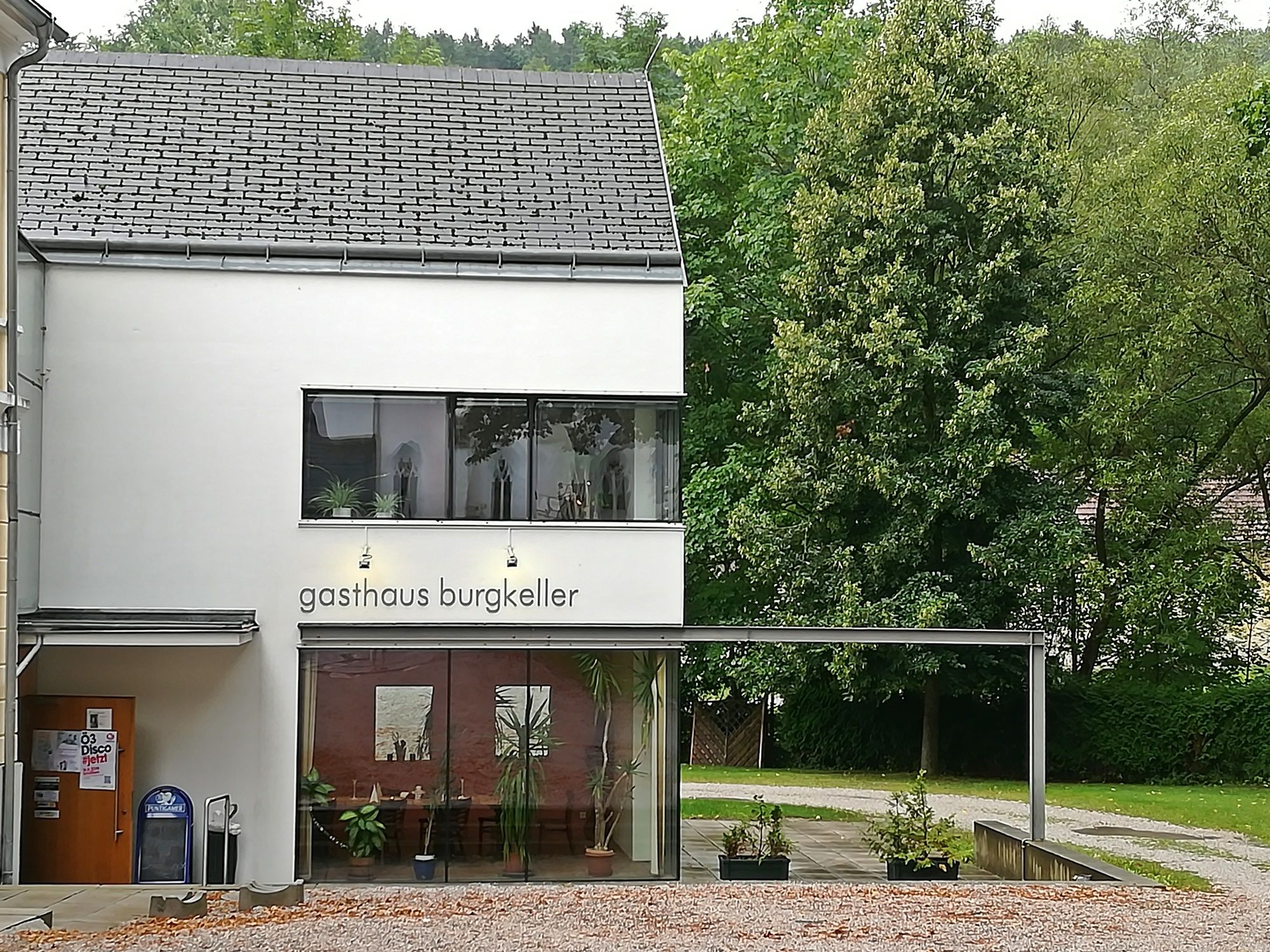 Modern building with the inscription 'Gasthaus Burgkeller', surrounded by trees.