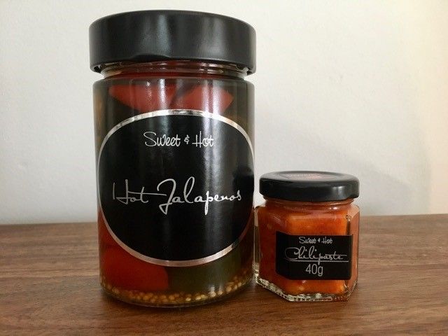 Ein Glas mit Jalapeños und ein kleines Glas mit Chilipaste auf einem Holztisch.