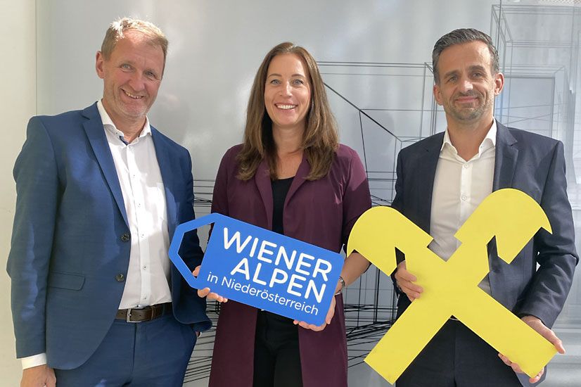  Dir. Johann Sperhansl (Raiffeisenbank Region Wiener Alpen), Wiener Alpen Geschäftsführerin Mariella Klement-Kappeller & Dir. Hannes Wedl (Raiffeisenbank Region Wiener Alpen) stehen für ein Gruppenbild nebeneinander und halten ein Wiener Alpen-Logo-Schild sowie ein Raiffeisen-Logo Schild in den Händen  