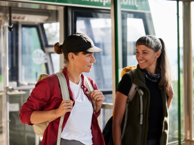 Zwei Wanderinnen stehen fröhlich am Ausgangspunkt ihrer Tour, umgeben von der majestätischen Kulisse der Wiener Alpen. Die frische Bergluft und die Vorfreude auf das Abenteuer in der Natur schaffen eine einladende Atmosphäre für alle, die die Schönheit der Berge erleben möchten.