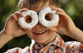 A boy holds two doughnuts sprinkled with powdered sugar in front of his eyes.