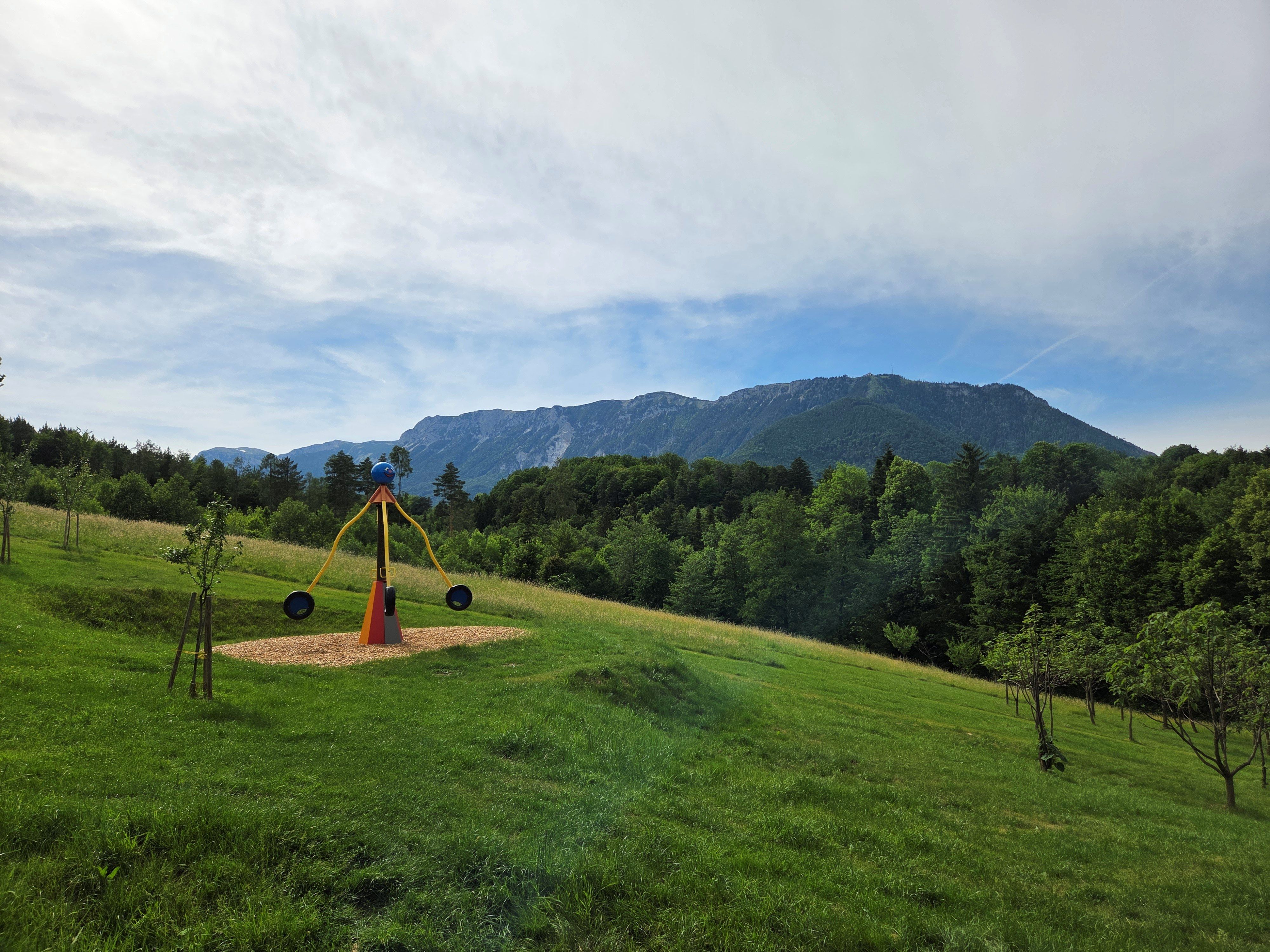 Ein Kinderspielplatz mit einer Wippe vor einer Berglandschaft mit der Rax im Hintergrund.
