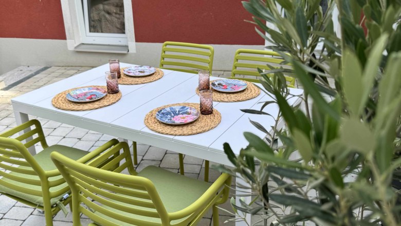 Terrasse mit gr&uuml;nem Stuhl, wei&szlig;em Tisch und roter Hauswand.