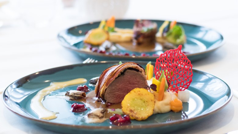 An artfully arranged dish of saddle of venison on a blue plate, decorated with vegetables.
