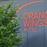 Logo des Orange Wings Hotels auf einer Wand mit Pflanzen im Vordergrund.