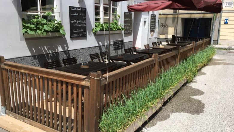 Outdoor area of a restaurant with wooden fence, tables and red parasols.